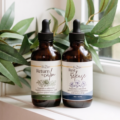 Complete Calm Duo. Two amber glass dropper bottles with white labels sit on a windowsill, surrounded by green leaves.